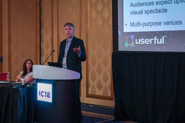 Tim Griffin, directeur technique d'Userful, donne une présentation sur l'AV sur IP à Infocomm 2018, avec Marielle Crisanti de Matrix Video Communications en arrière-plan.