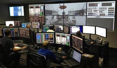 Une salle de contrôle avec des travailleurs à leur poste de travail et un mur vidéo affichant des images et des données en direct.