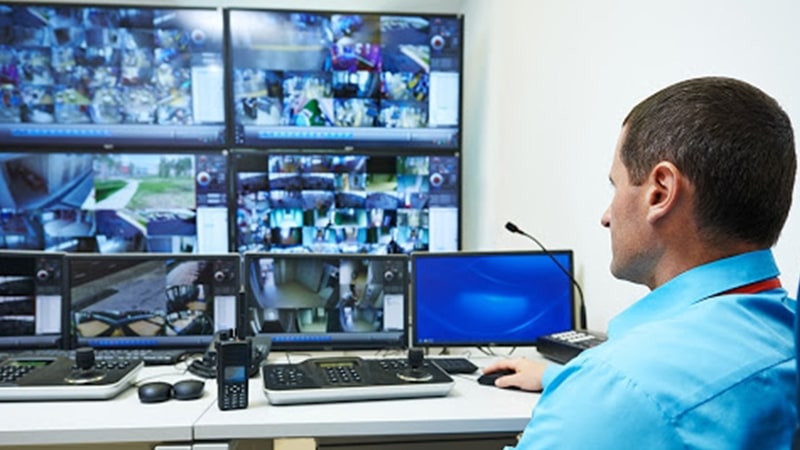 Un homme dans le centre de contrôle de la sécurité du campus surveille le campus par le biais d'un mur vidéo affichant les images des caméras en direct.