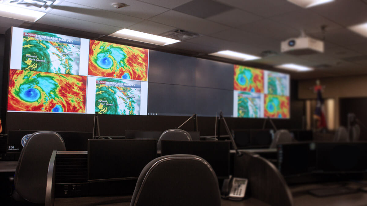 Salle de contrôle vide avec radars météorologiques affichés sur un grand mur vidéo, et postes de travail
