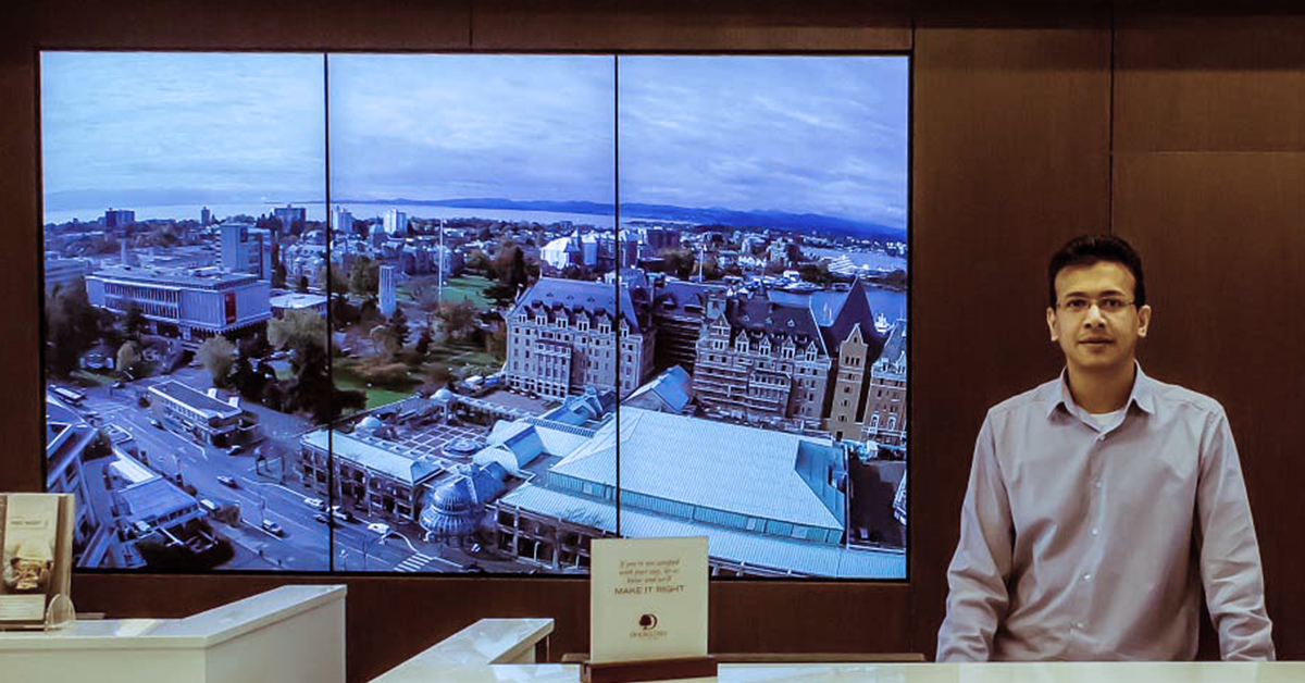 Réceptionniste du DoubleTree by Hilton et mur vidéo à 3 panneaux derrière lui, affichant des points de repère de Victoria, au Canada.