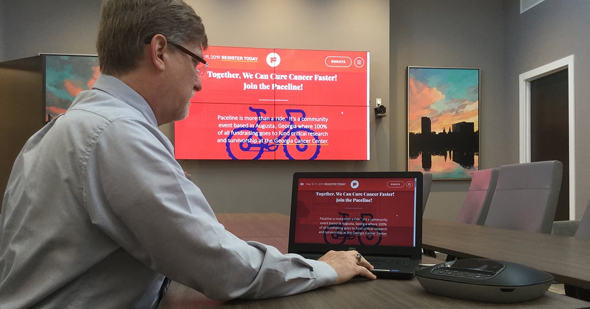 Salle de réunion du Medical College of Georgia, avec un homme utilisant son ordinateur portable et Userful pour afficher une page web sur un mur vidéo derrière lui