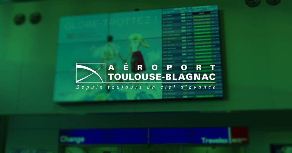 Mur vidéo à l'aéroport de Toulouse-Blagnac affichant l'annonce et les heures de départ des vols avec une superposition verte et un logo.