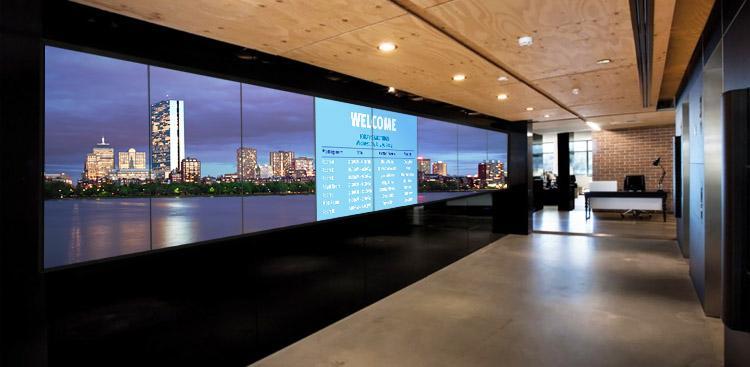 Hall d'entrée d'un bureau vide, avec un grand mur vidéo affichant une bannière de bienvenue et une photo de l'horizon d'une ville.