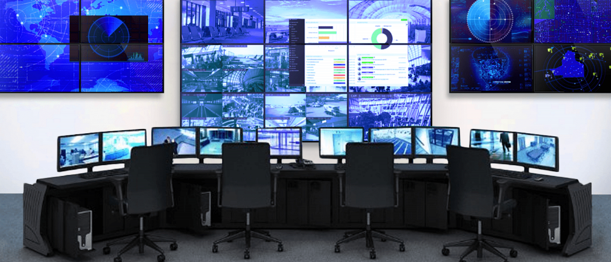 Salle de contrôle vide avec 4 postes de travail et 3 murs vidéo affichant les images des caméras de sécurité en direct et les tableaux de bord des données.