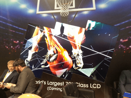 Deux personnes discutent devant un mur vidéo artistique où les écrans sont en angle et montrent de façon continue l'image d'une personne jouant au basket.