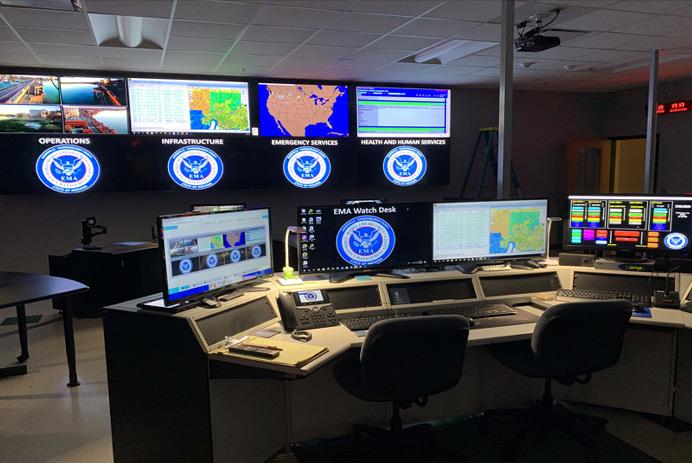 Salle de contrôle vide de l'EMA, avec un poste de travail et un mur vidéo affichant des photographies, des données et des cartes.