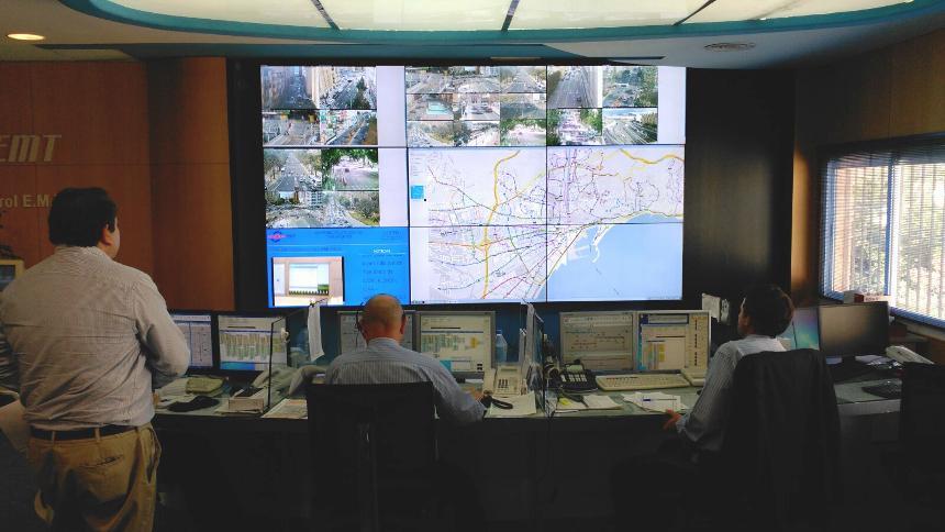 Centre de contrôle EMT avec des travailleurs qui surveillent les conditions de transit à partir de leurs postes de travail et un mur vidéo affichant les itinéraires de transit, les images en direct et les données.