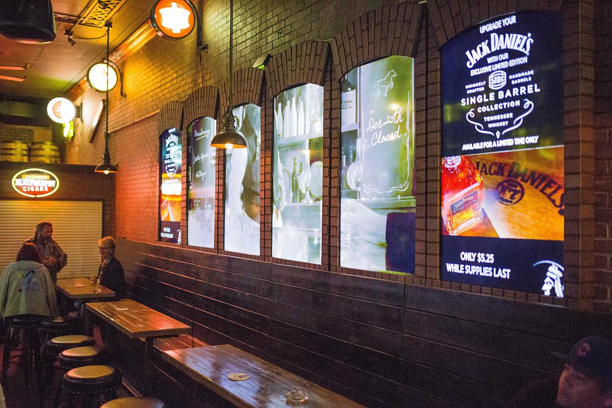 Murs vidéo de style fenêtre dans le Smokin' Joe's Pub, affichant des publicités et des œuvres d'art visuel.