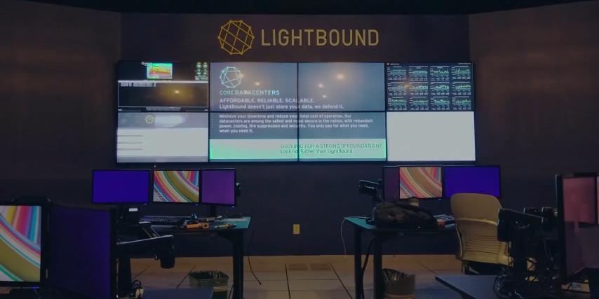 Salle de contrôle vide de Lightbound avec 2 postes de travail et un mur vidéo affichant des sites web, des données et des publicités.