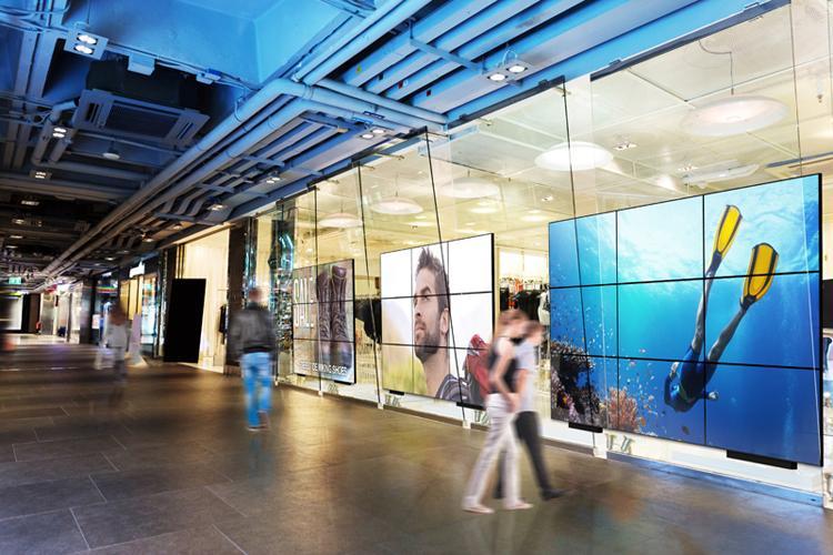 Plusieurs grands murs vidéo conviviaux dans le hall d'un centre commercial, affichant des publicités et des œuvres d'art.