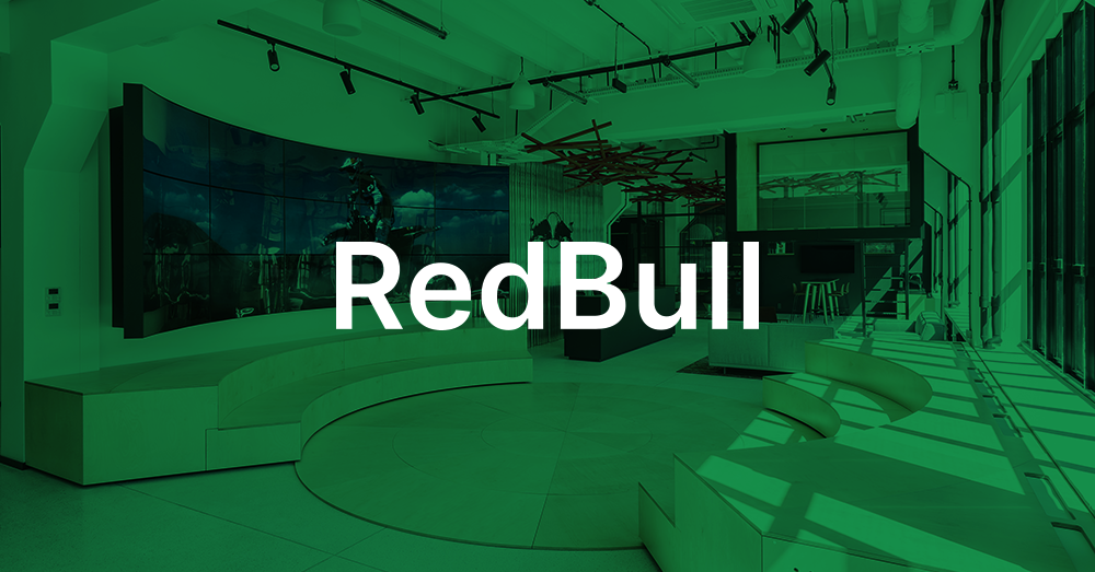 Lobby du siège social de Redbull Pologne, avec un escalier, un coin salon, un bureau de réception et un mur vidéo incurvé affichant une publicité Red Bull avec une superposition verte et le logo.