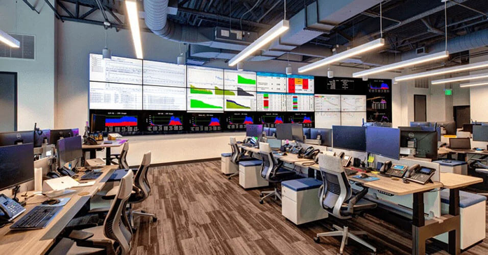 Centre d'exploitation du réseau SpectrumVoIP vide, avec de nombreux postes de travail et un grand mur vidéo affichant des tableaux de bord de données.